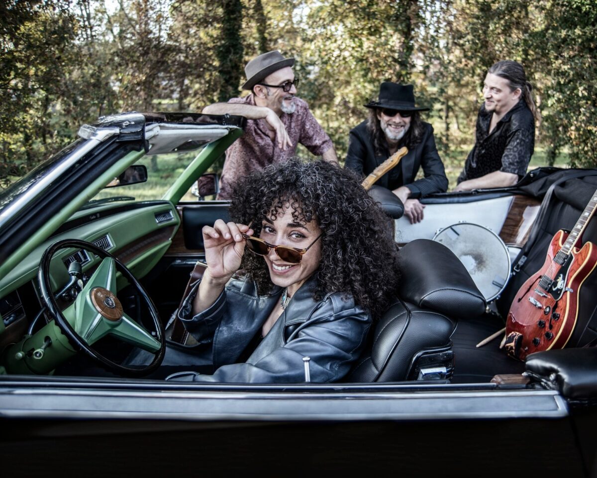 Sweet Marta & The Blues Shakers posan con un descapotable verde y una guitarra